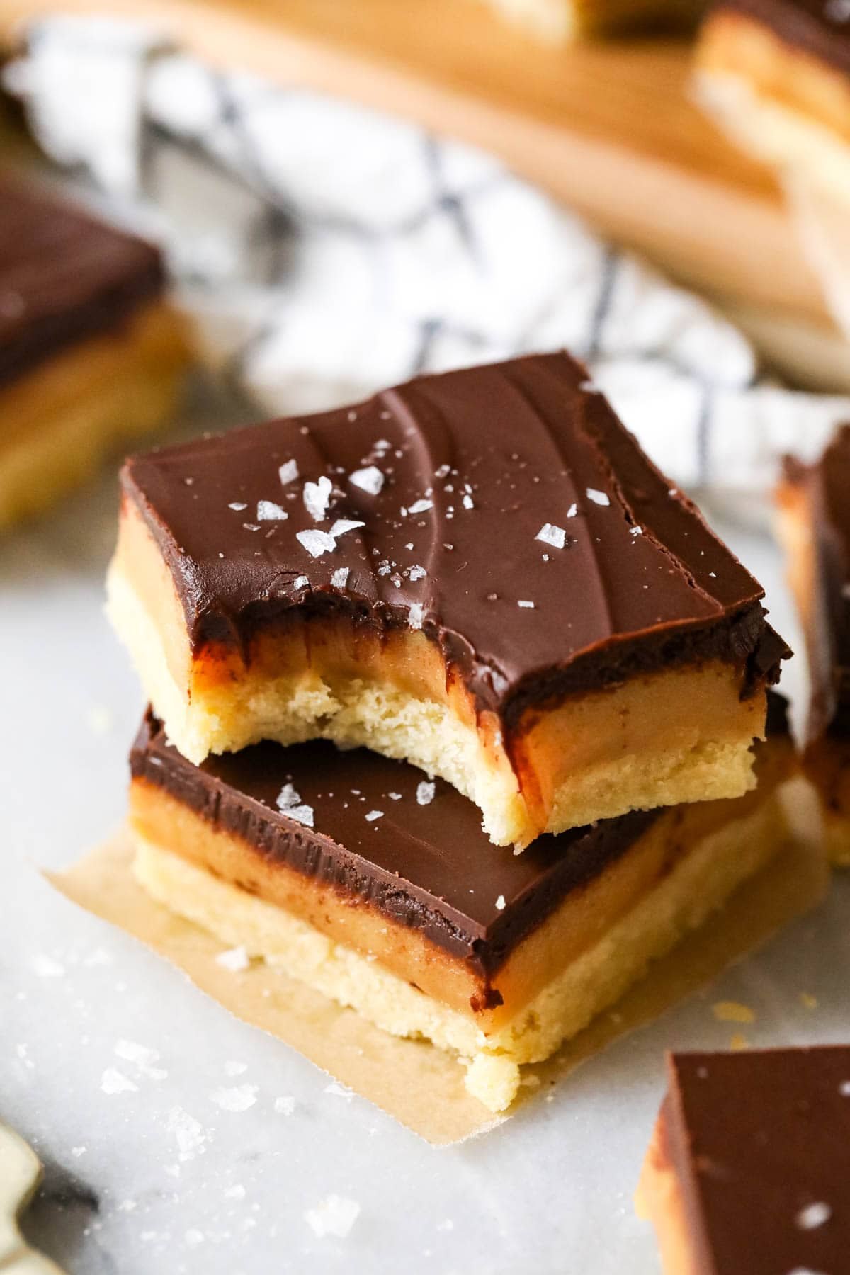 Two square slices of millionaire's shortbread topped on top each other, a bite missing to show chewy caramel center. Topped with sea salt.