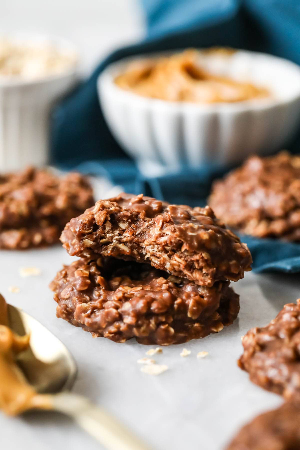 Two stacked chocolate no-bake cookies, one with a bite missing, small white dish of peanut butter in background.