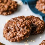 Two no bake cookies on marble with blue cloth in background.