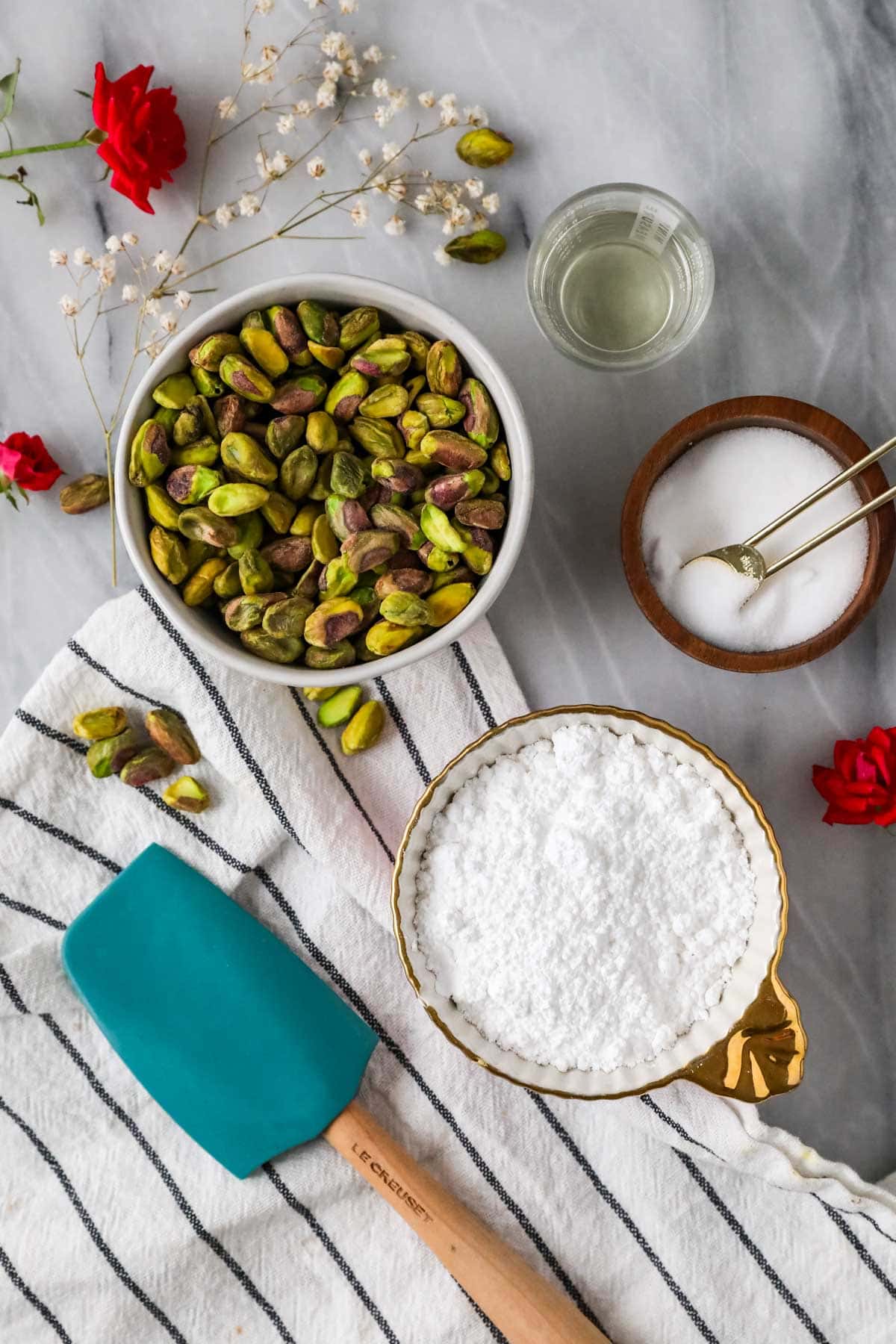 Overhead view of ingredients including pistachios, powdered sugar, salt, and oil.