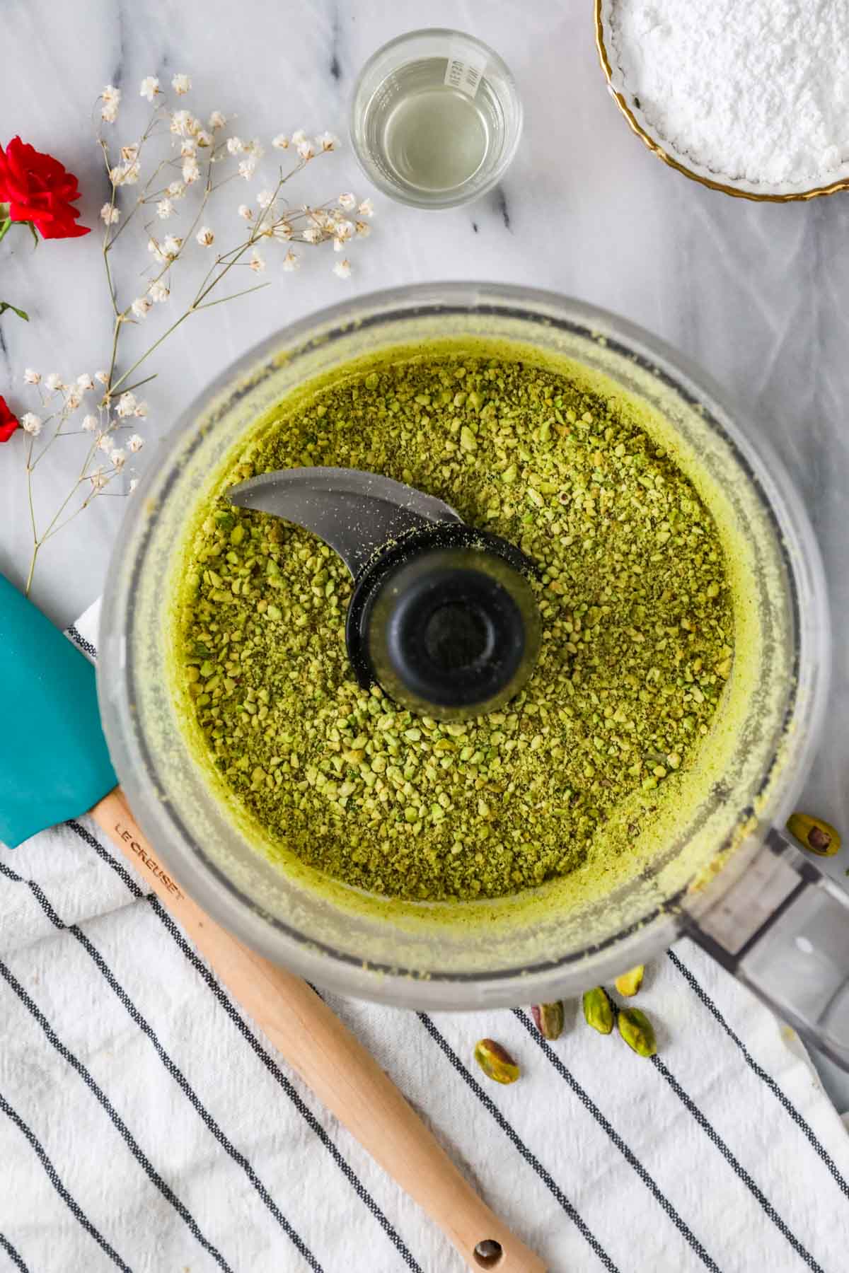 Overhead view of a food processor with pistachio crumbles inside.