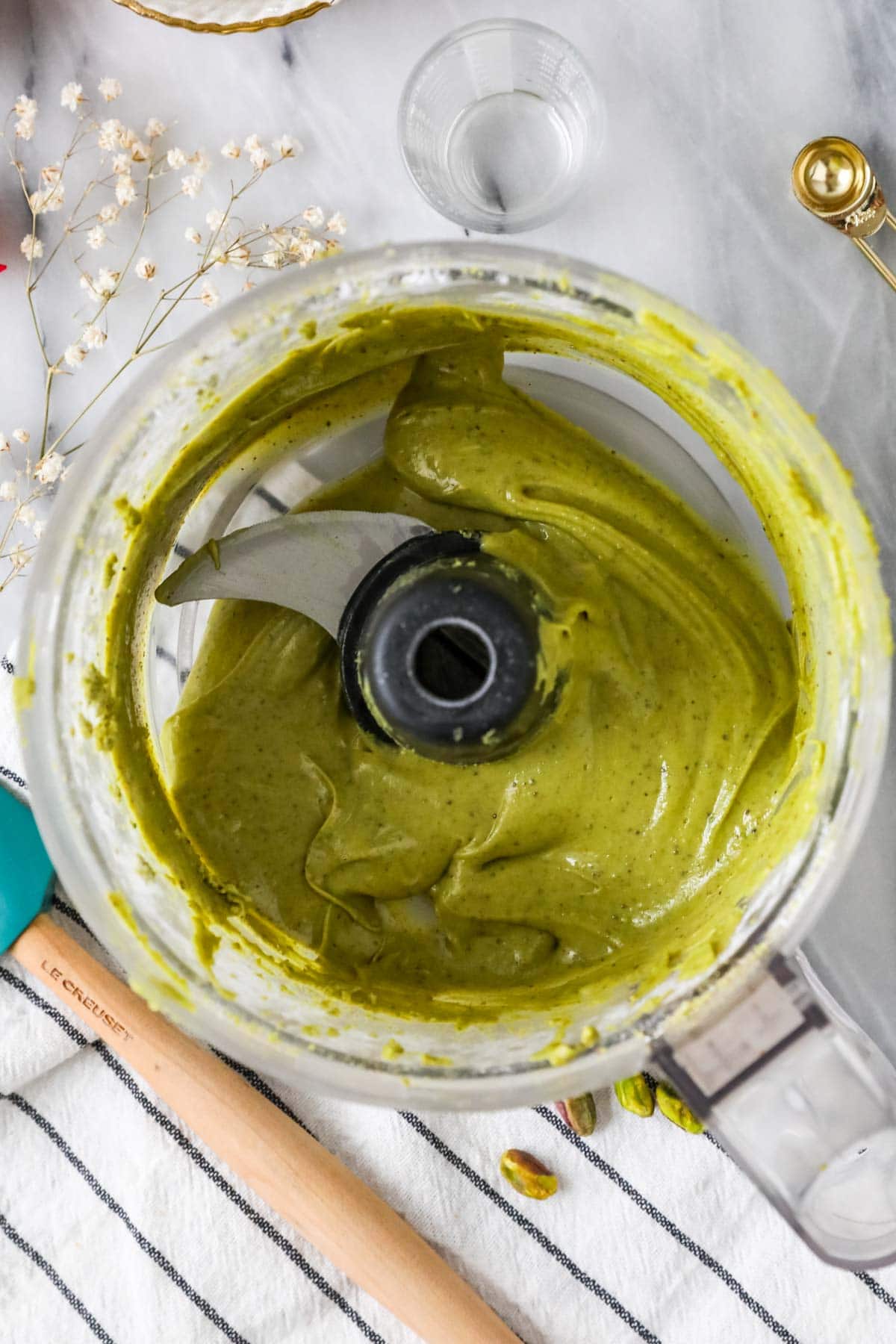 Overhead view of a food processor after blending pistachios, powdered sugar, oil, and salt into a cream.