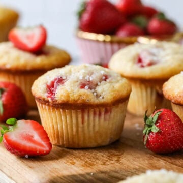 Strawberry muffins with sparkling sugar tops on a wood serving board.