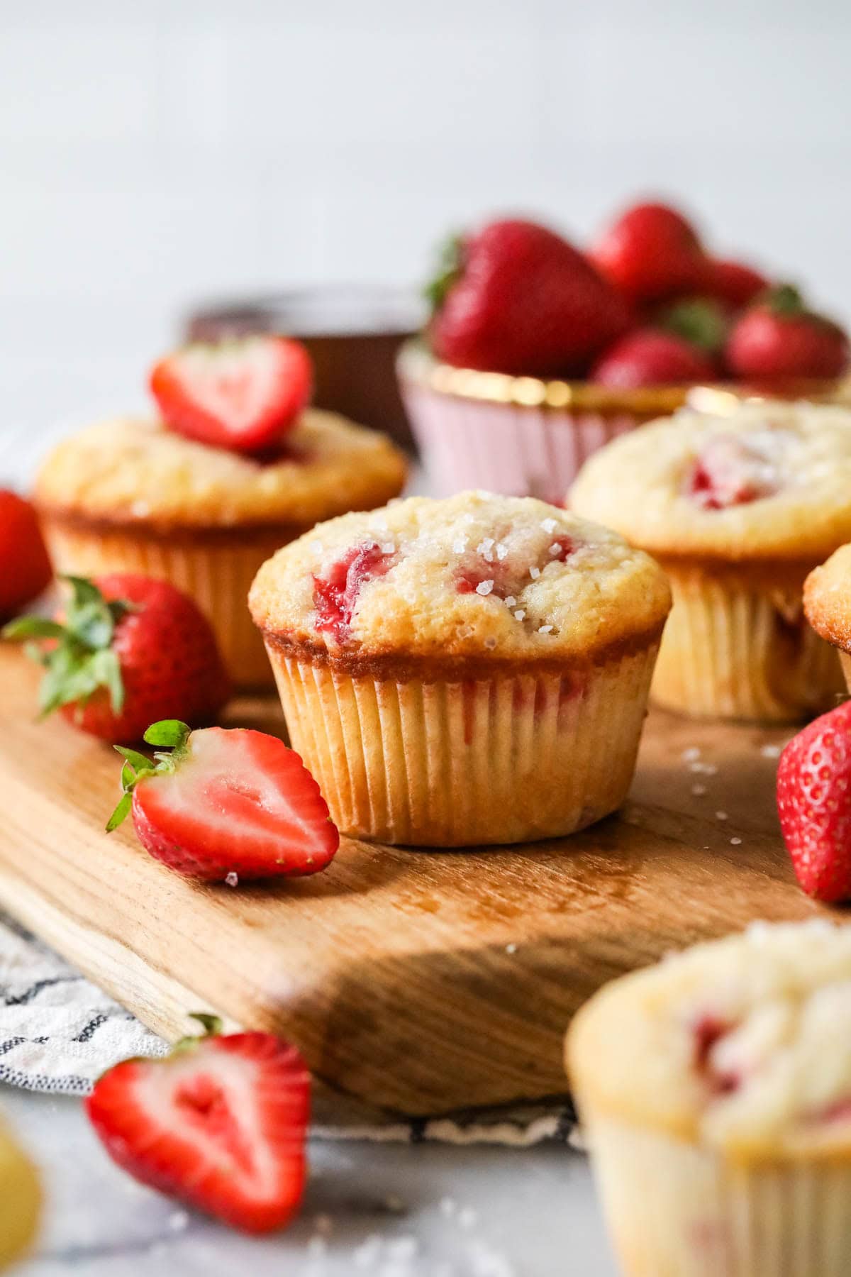 Strawberry muffins with sparkling sugar tops on a wood serving board.