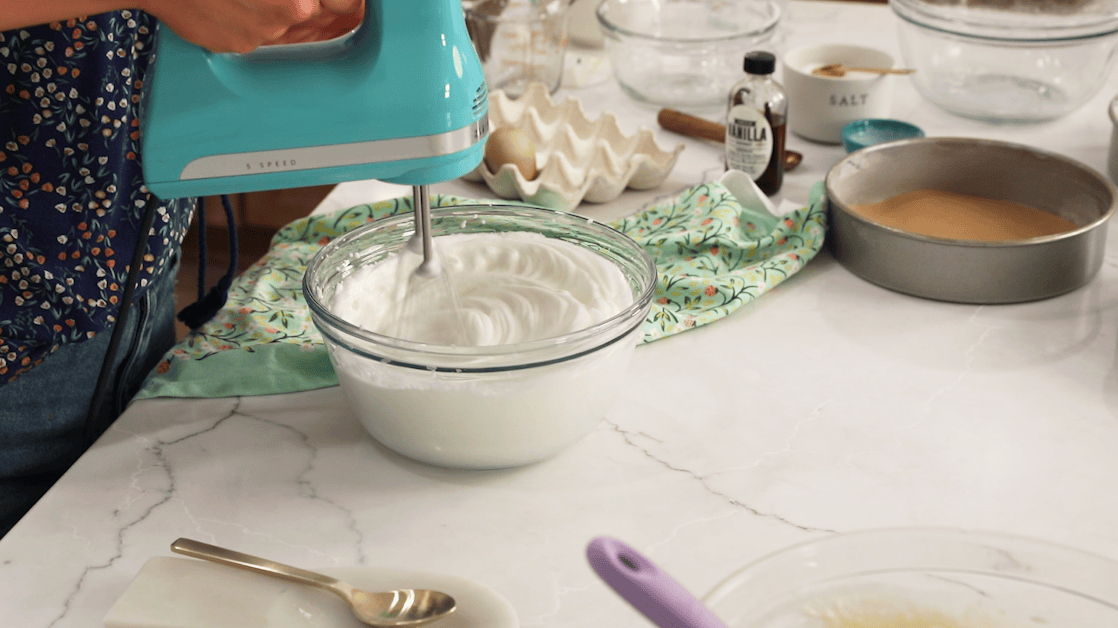 Egg whites being whipped into stiff peaks for vanilla cake layers.