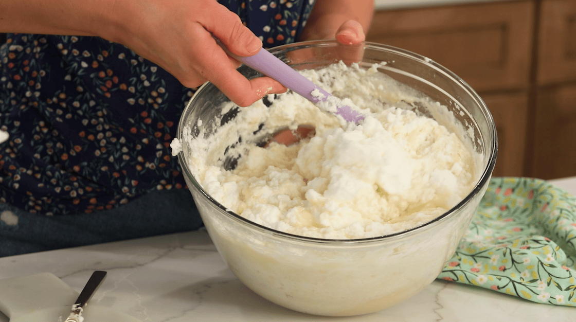 Egg whites being folded into cake batter for fluffy cake layers.