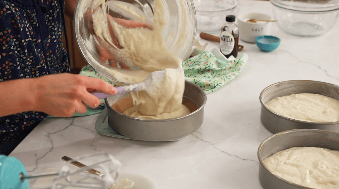 Cake batter being divided between three round pans.