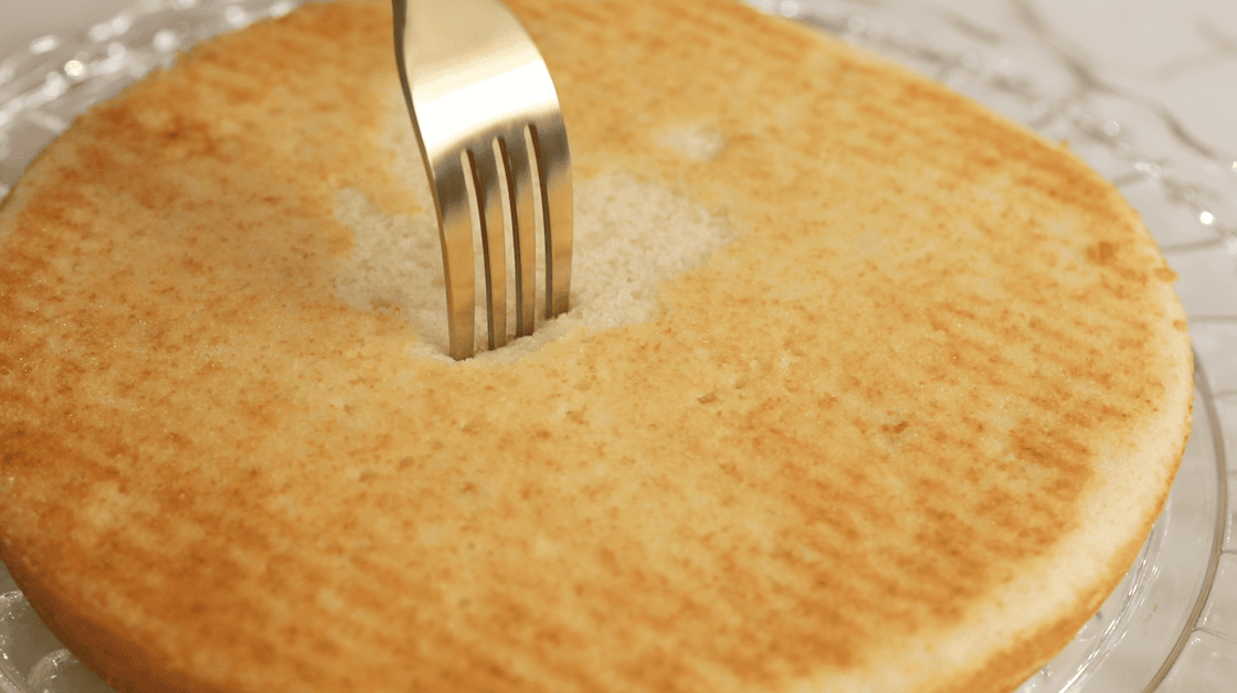 Fork poking cake layer in preparation for simple syrup.