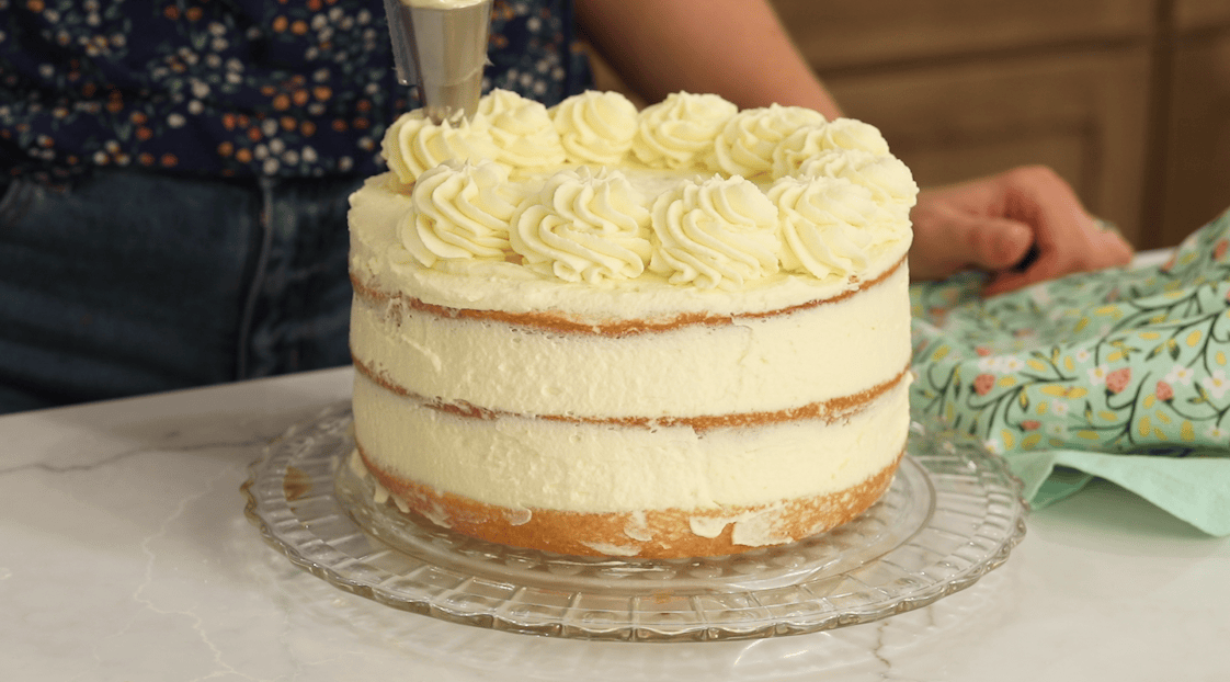 Piping frosting dollops around the edge of a tiramisu layer cake that's been lightly frosted.