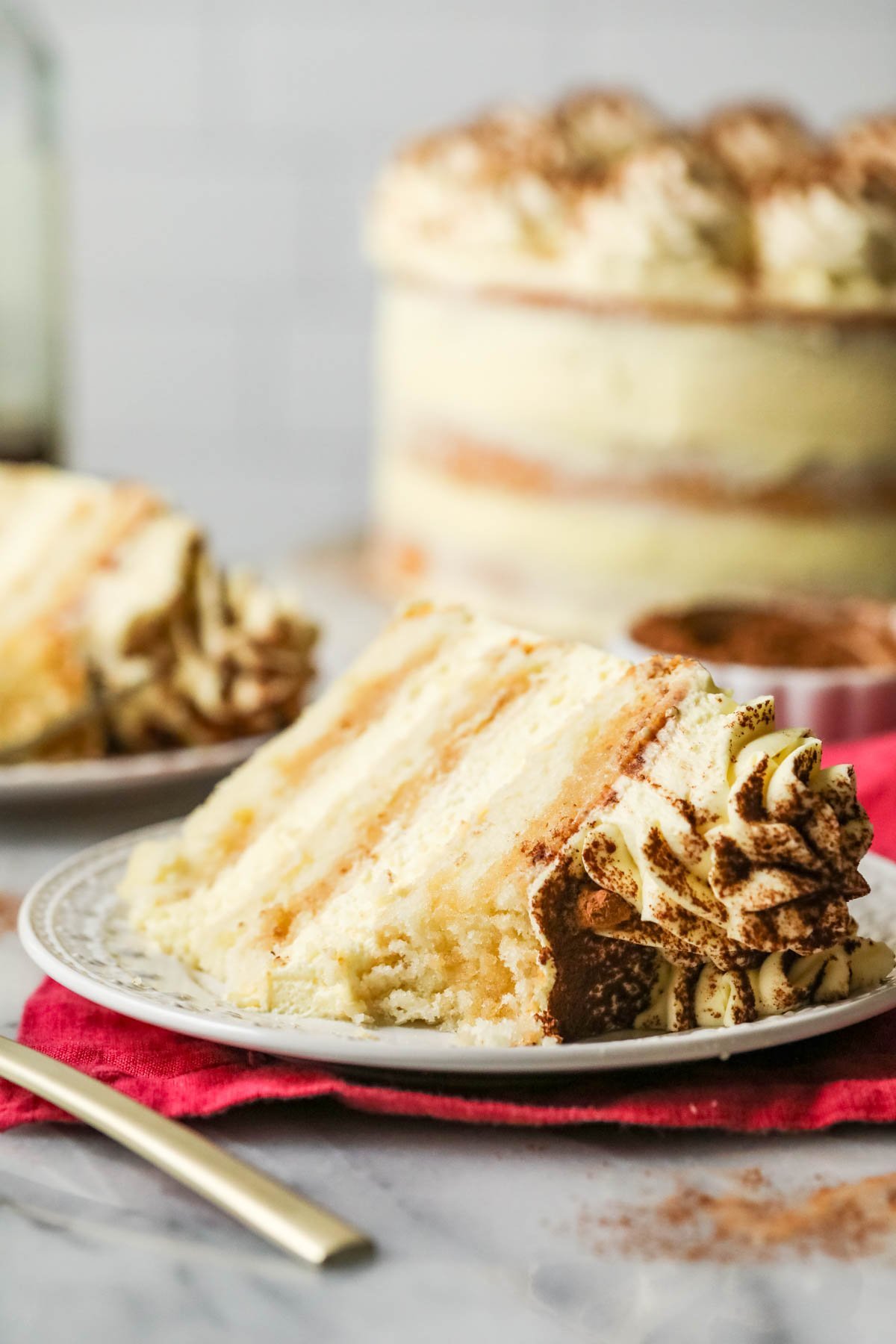 Slice of tiramisu layer cake with one bite missing on a plate.