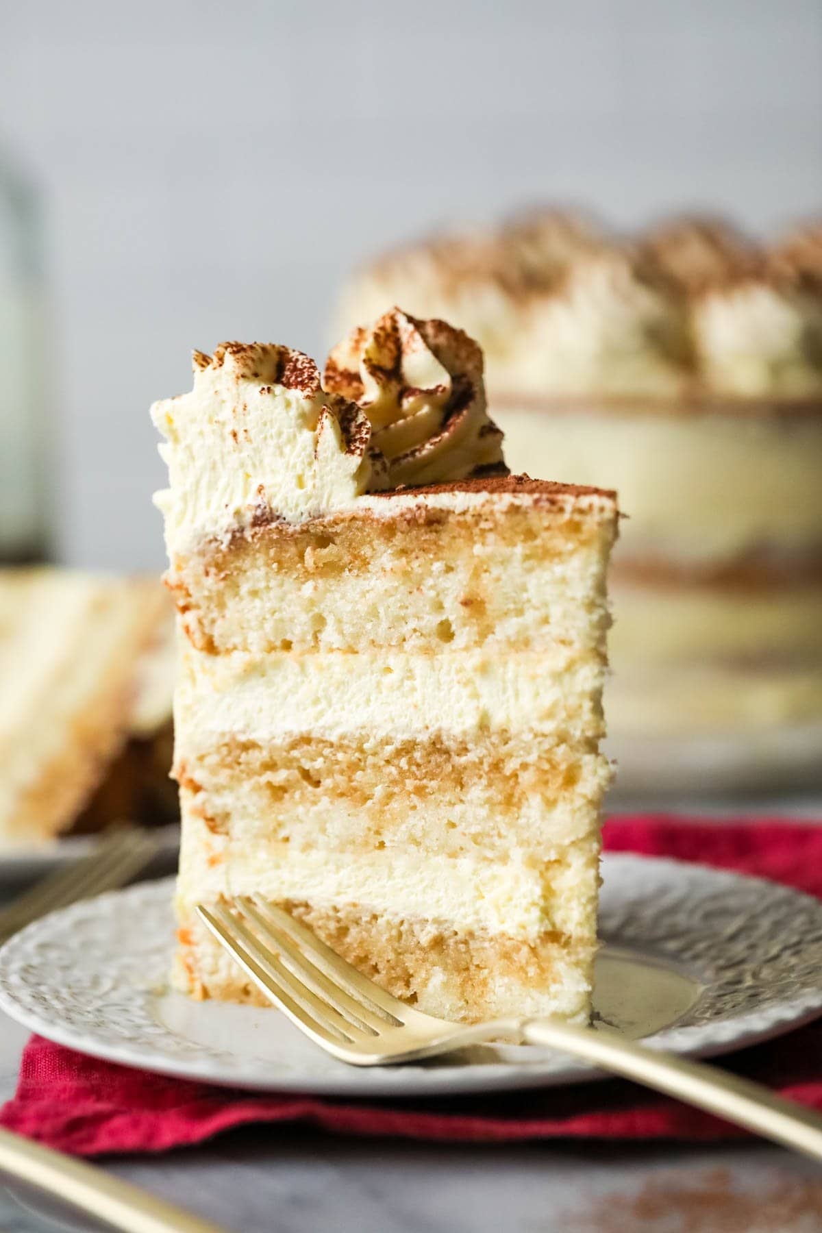 Tall slice of tiramisu cake on a plate with a fork beside it.