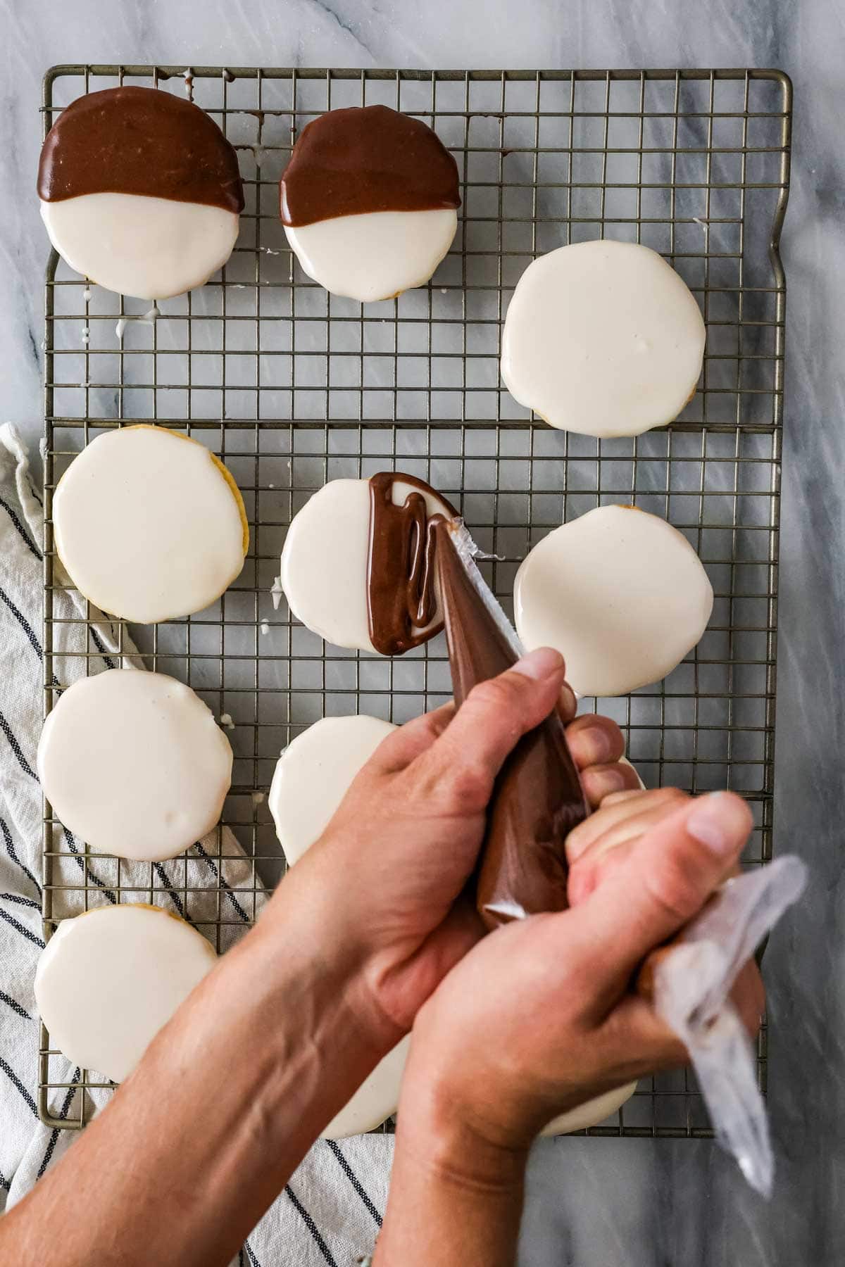 Overhead view of chocolate frosting being piped over just half of each white frosted cookie.