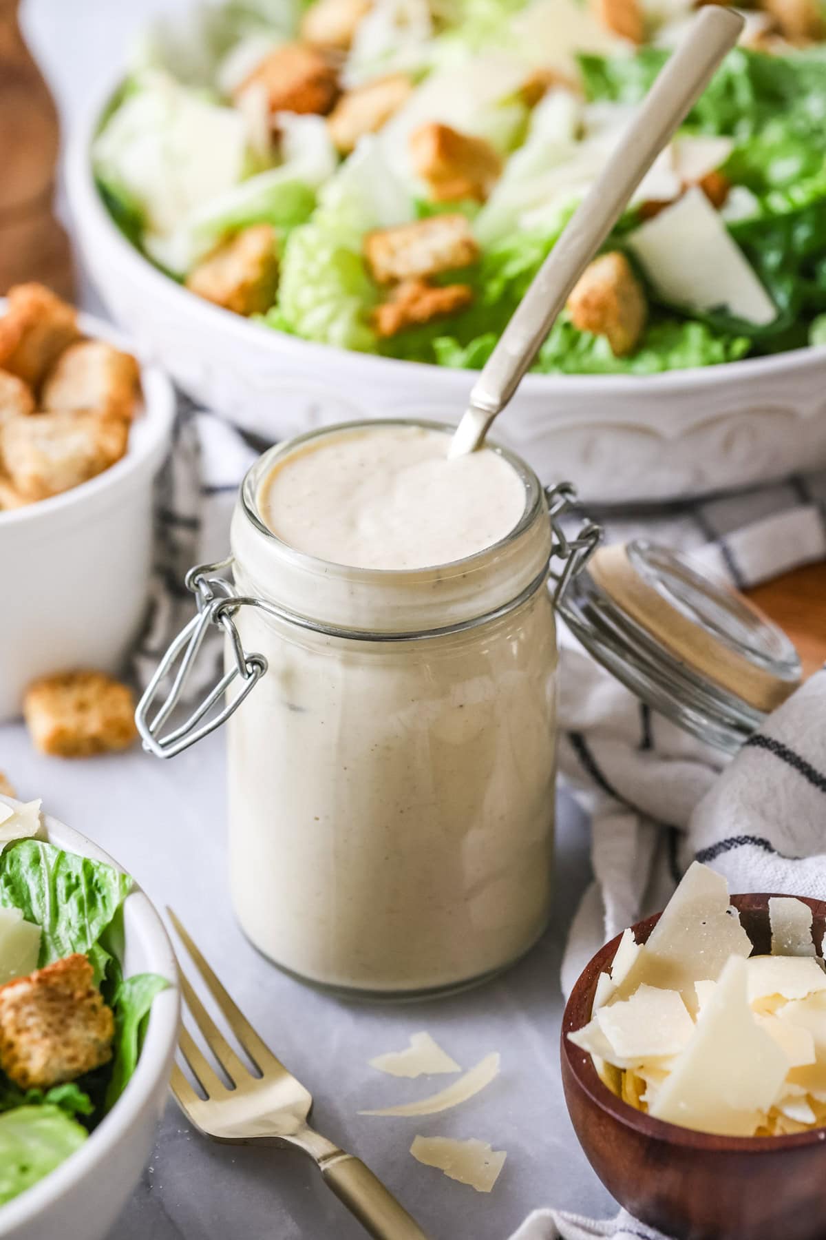 Spoon in a jar of homemade caesar dressing with salads in the background.