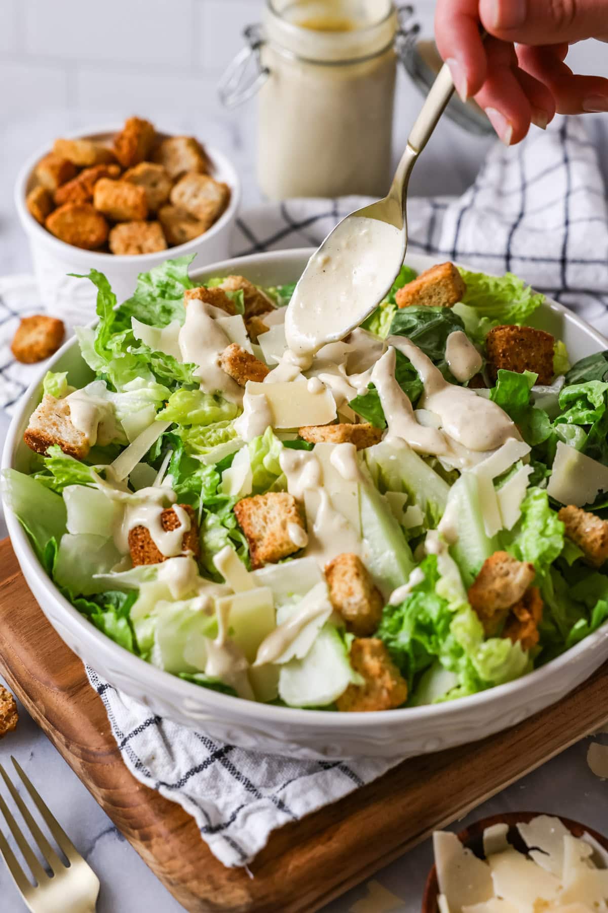 Caesar dressing being drizzled over a caesar salad.