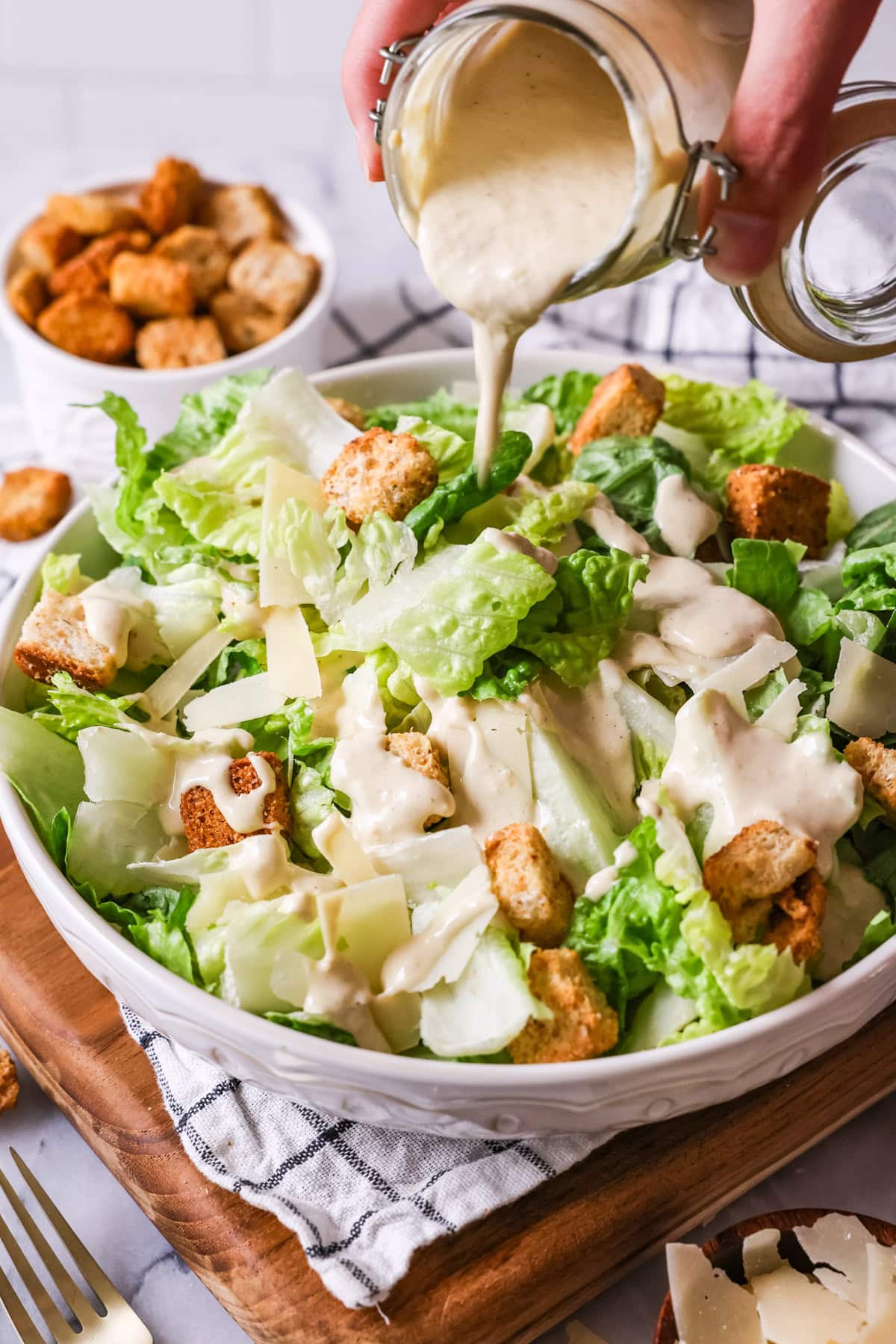 Caesar dressing being drizzled over a caesar salad.