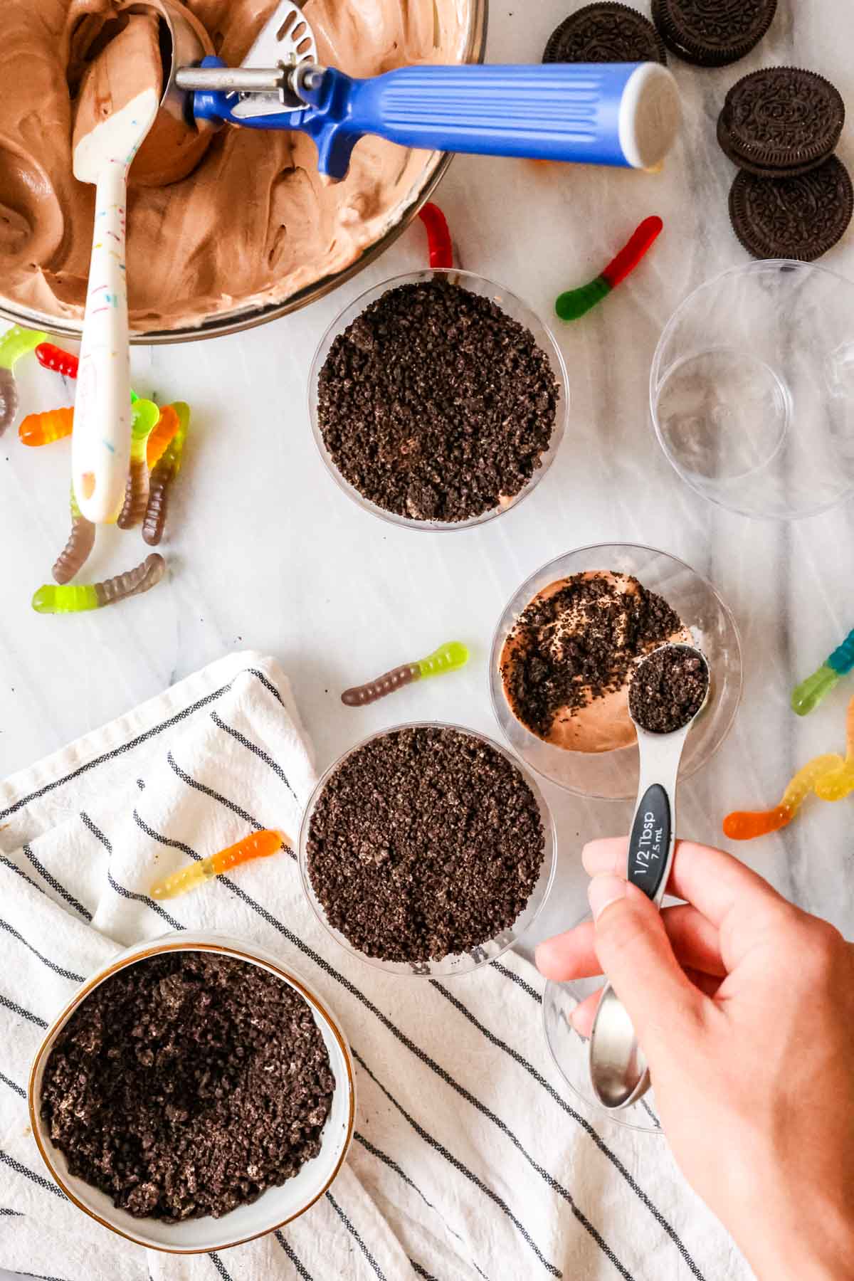 Overhead view of Oreo crumbs and fluffy chocolate pudding being layered into cups to make dirt pudding.