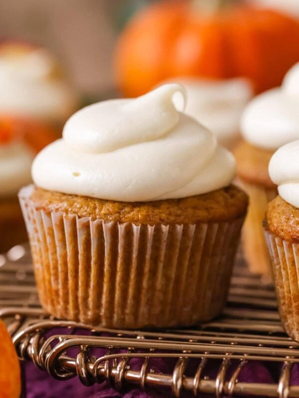 Pumpkin cupcake topped with a brown sugar cream cheese frosting on a cooling rack.