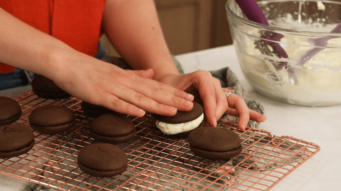Pressing two chocolate cookie shells together with a creamy filling in between.