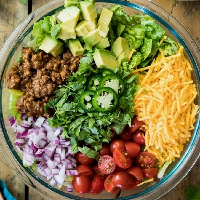 Overhead view of a bowl of salad topped with taco meat, cheese, avocado, and more.