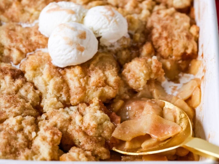 Spoon scooping a serving of apple cobbler from a baking dish.