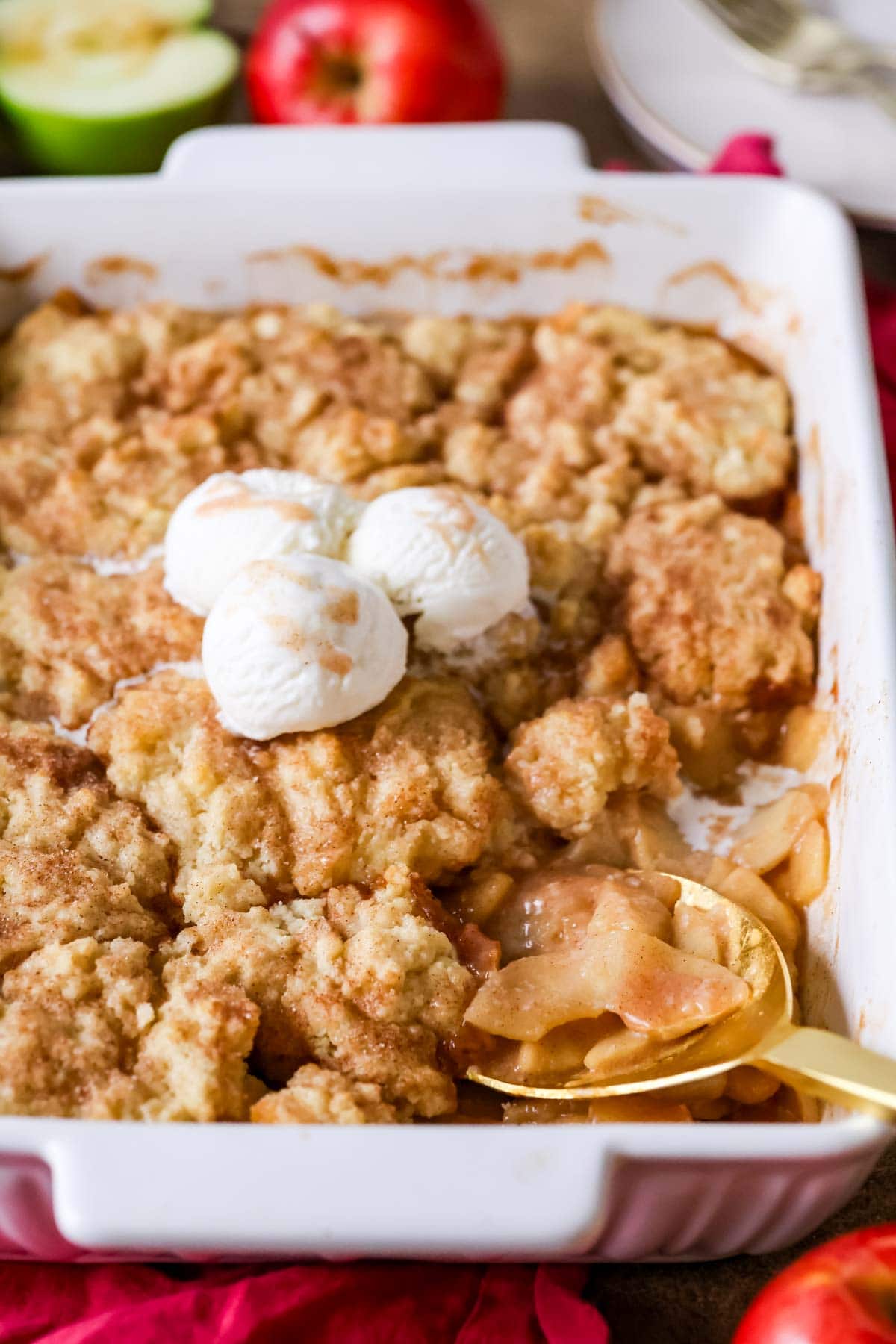 Spoon scooping a serving of apple cobbler from a baking dish.