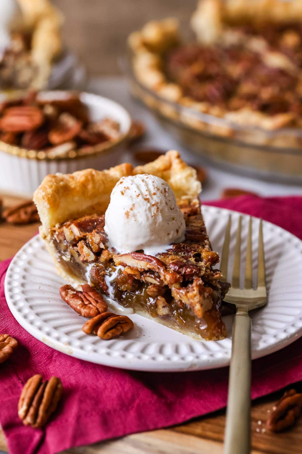 Slice of pecan pie topped with vanilla ice cream on a plate.