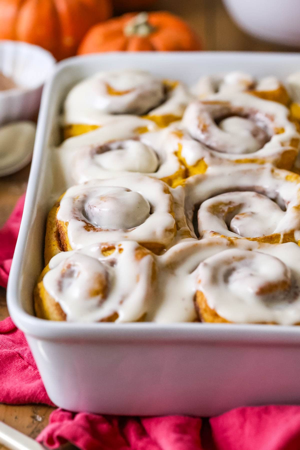 Dish of pumpkin cinnamon rolls frosted with cream cheese frosting.