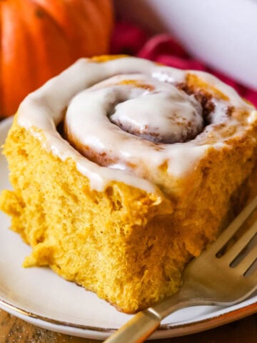 Pumpkin cinnamon roll frosted with cream cheese icing on a plate.