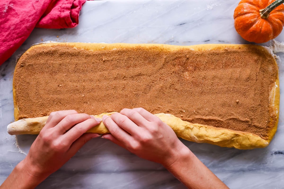 Pumpkin cinnamon roll dough being rolled up into a log.