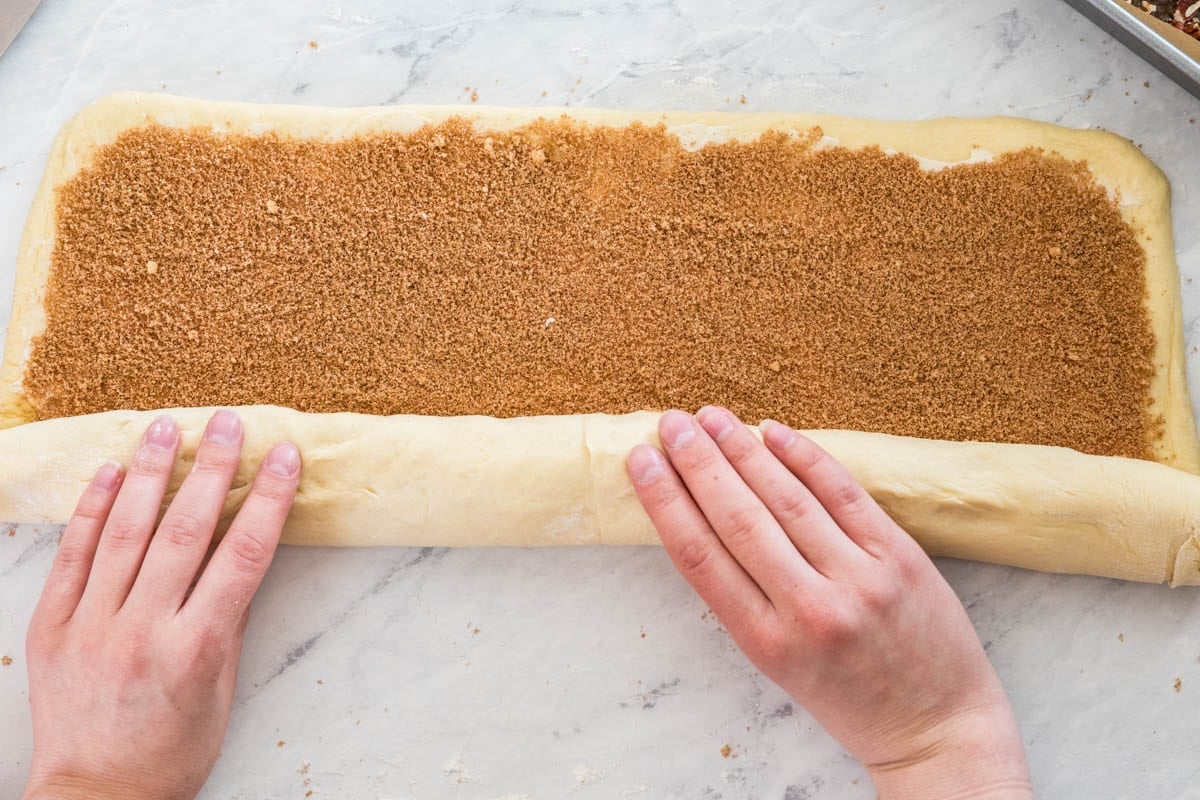 Rolling cinnamon-sugared dough for sticky buns into tight log.