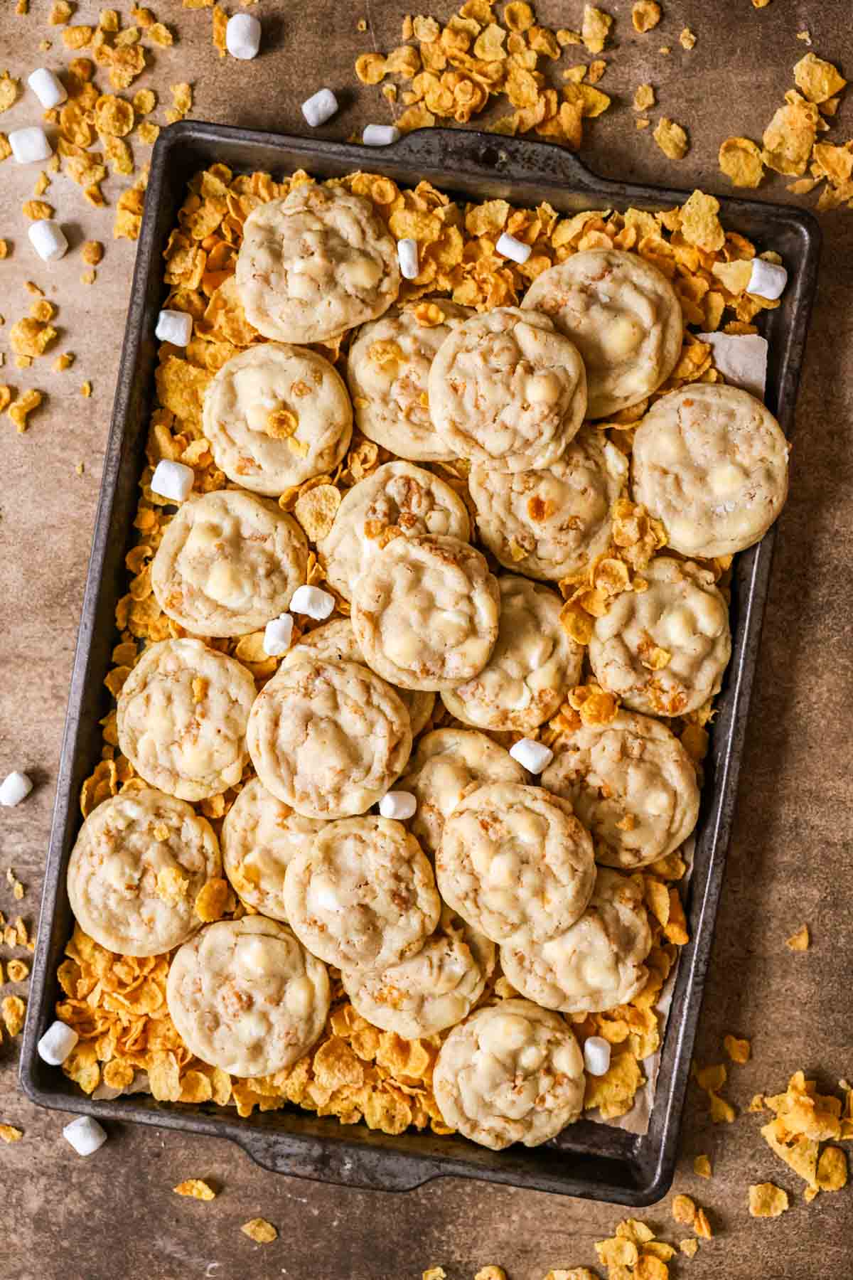Overhead view of cornflake cookies surrounded by cornflakes and mini marshmallows.