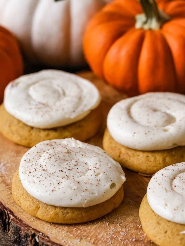 4 Pumpkin Cookies with Cream Cheese Frosting, orange pumpkins in the background.