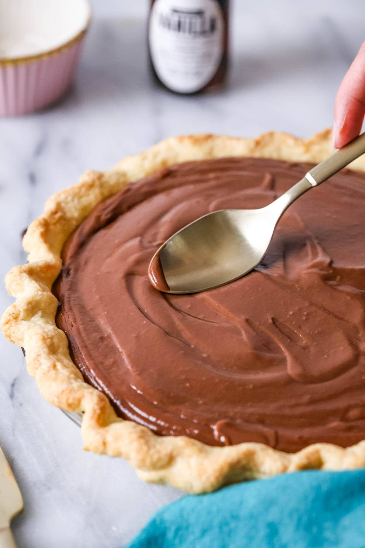 Spoon smoothing a chocolate custard filling into a pie crust.