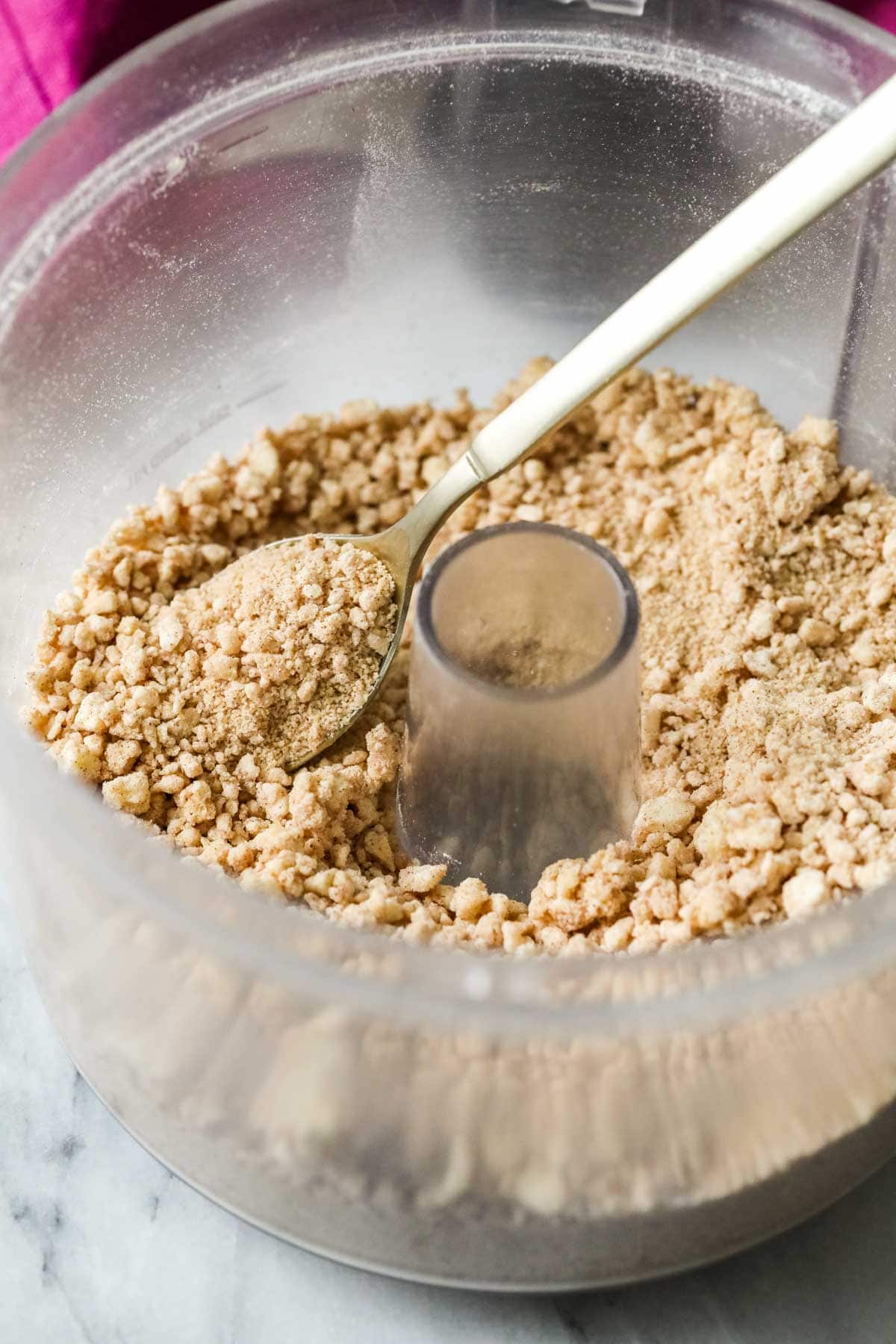 Close-up view of a crumb topping in a food processor bowl.