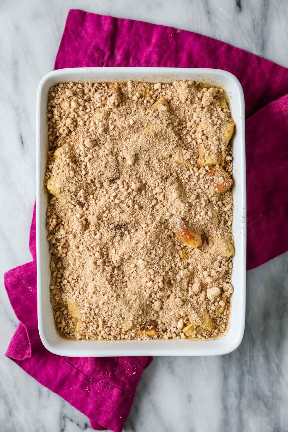 Overhead view of a casserole dish of bread and custard topping with a streusel topping before baking.
