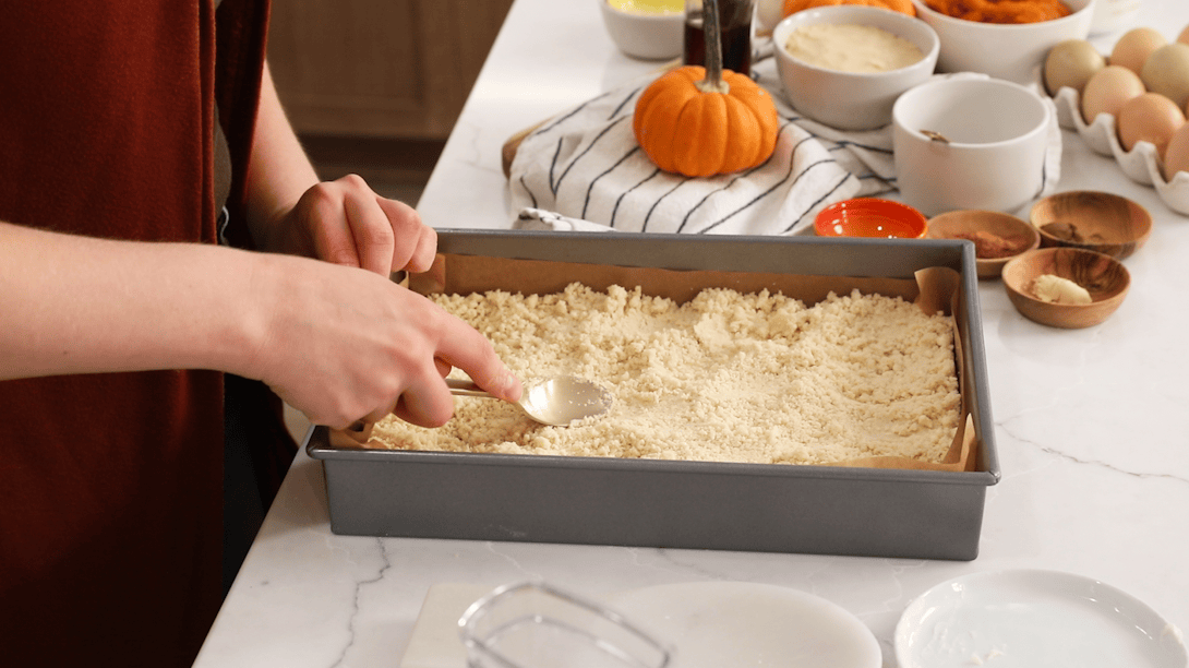 Spoon smoothing a shortbread crust into a baking pan.