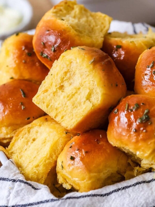 Pile of golden brown sweet potato dinner rolls topped with a garlic rosemary butter.