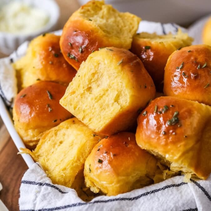 Pile of golden brown sweet potato dinner rolls topped with a garlic rosemary butter.