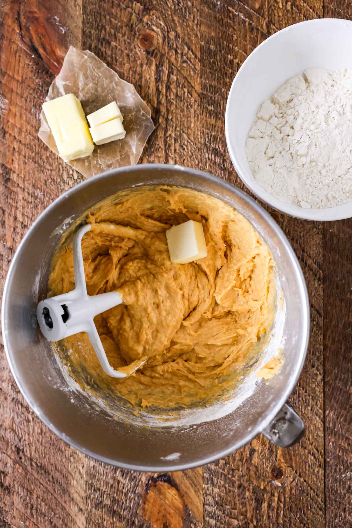 Overhead view of a butter being added to a sweet potato dough.