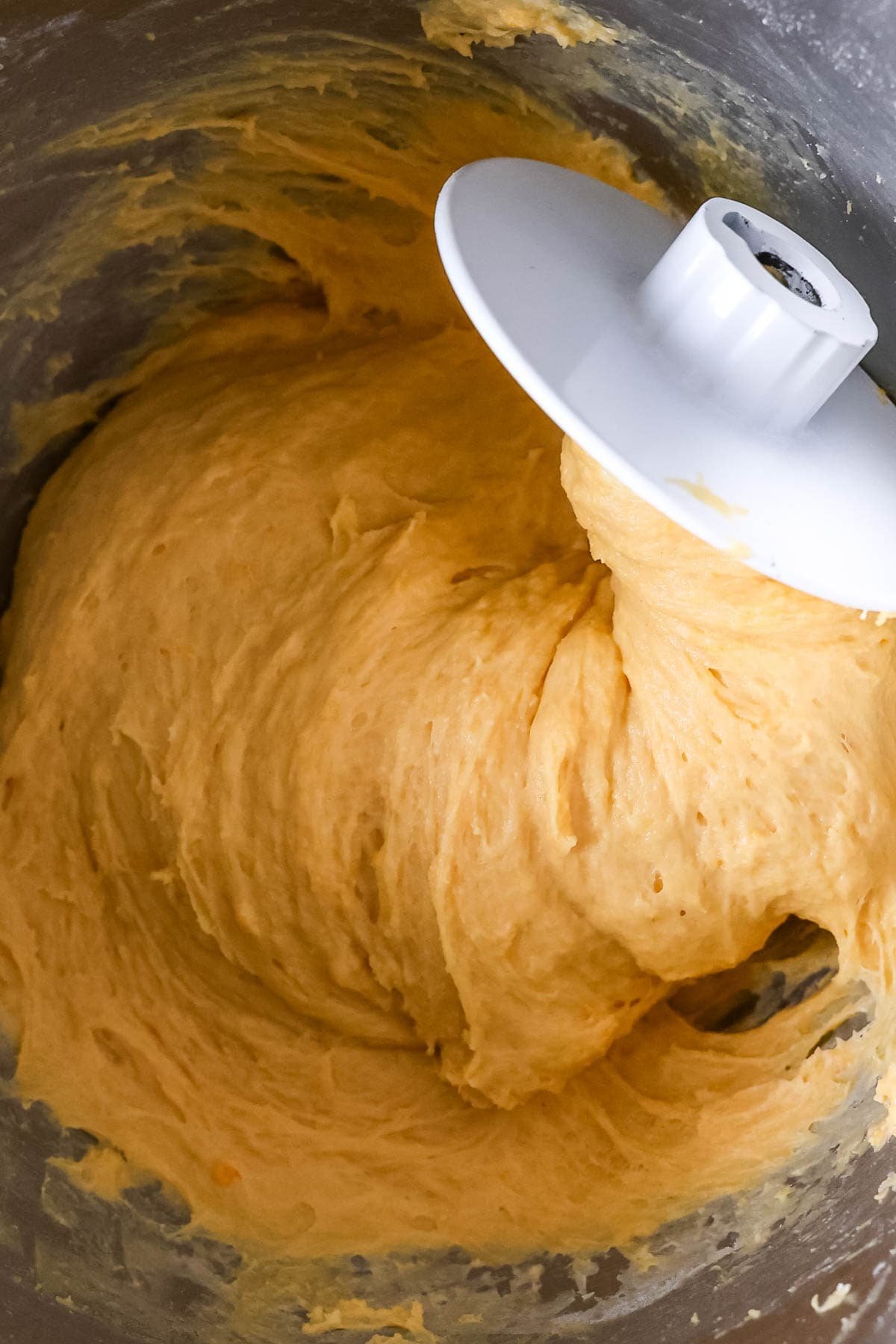 Close-up view of an orange tinted dough on a dough hook.