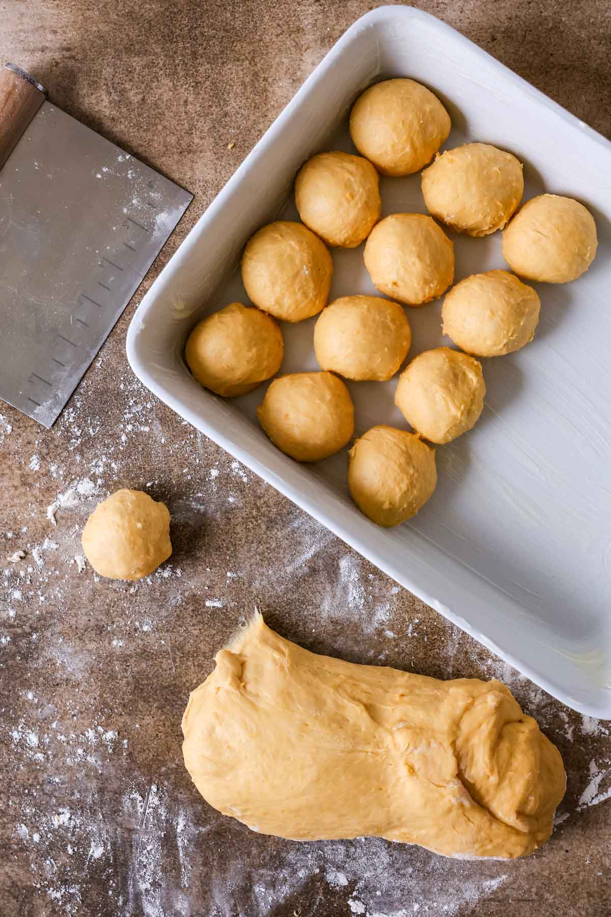 Overhead view of a sweet potato infused dough being formed into round balls in a baking dish.