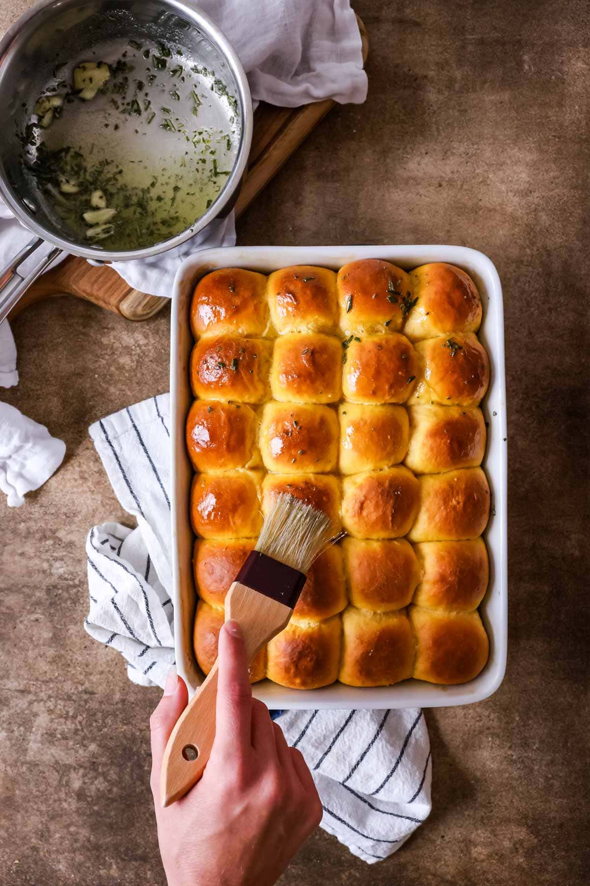 Rosemary butter being brushed over sweet potato dinner rolls.