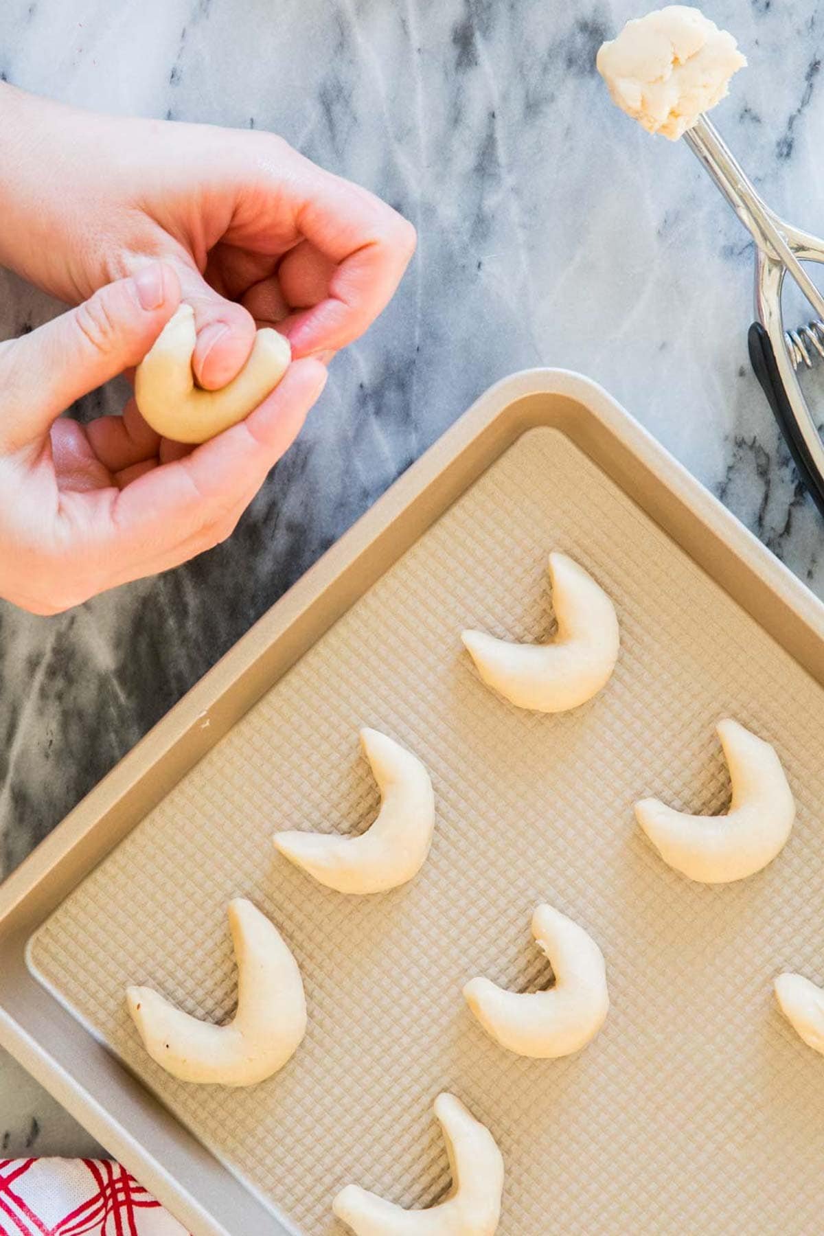 Hands forming cookie dough into crescent moon shapes.