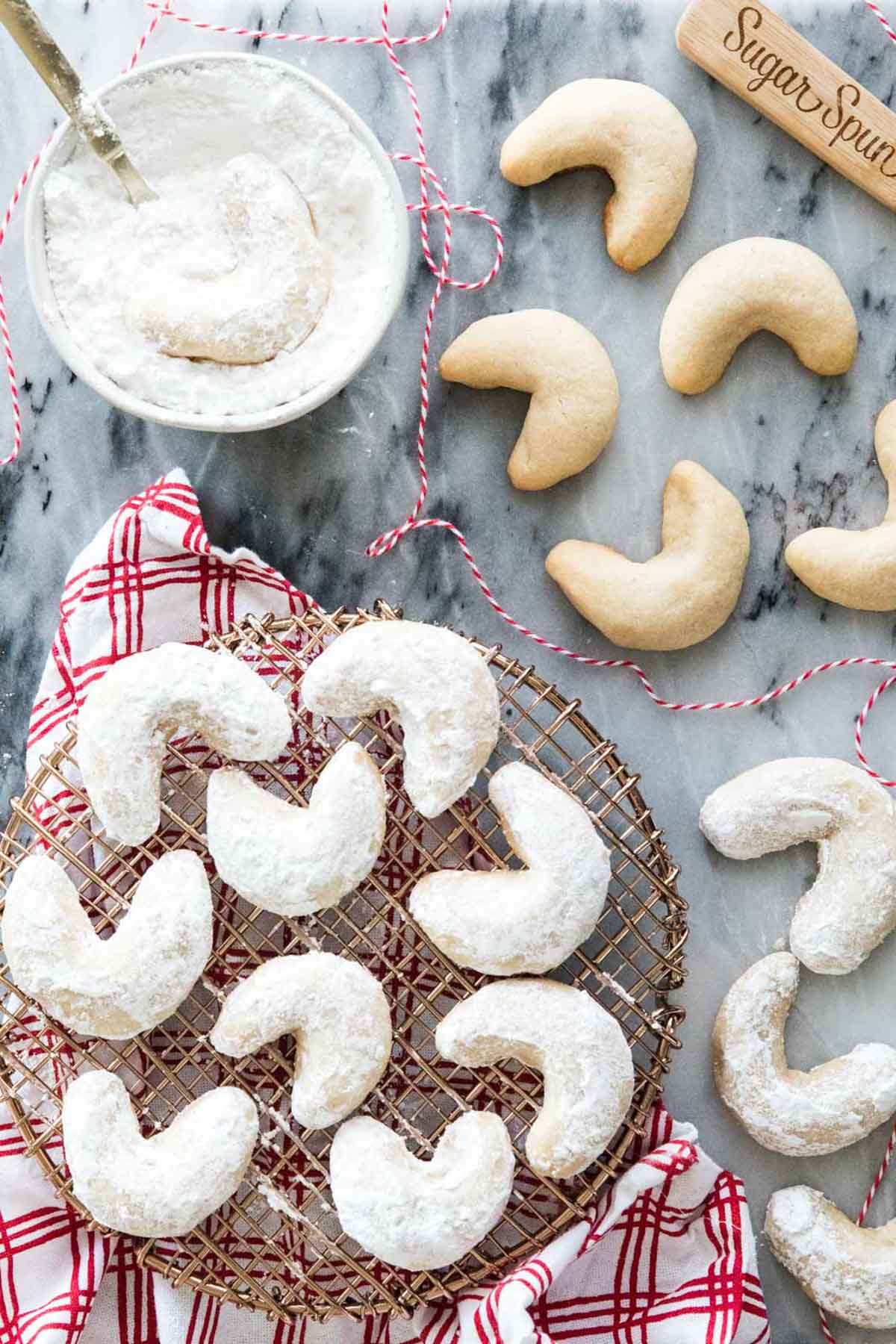 Overhead view of crescent moon shaped cookies being dipped in powdered sugar.