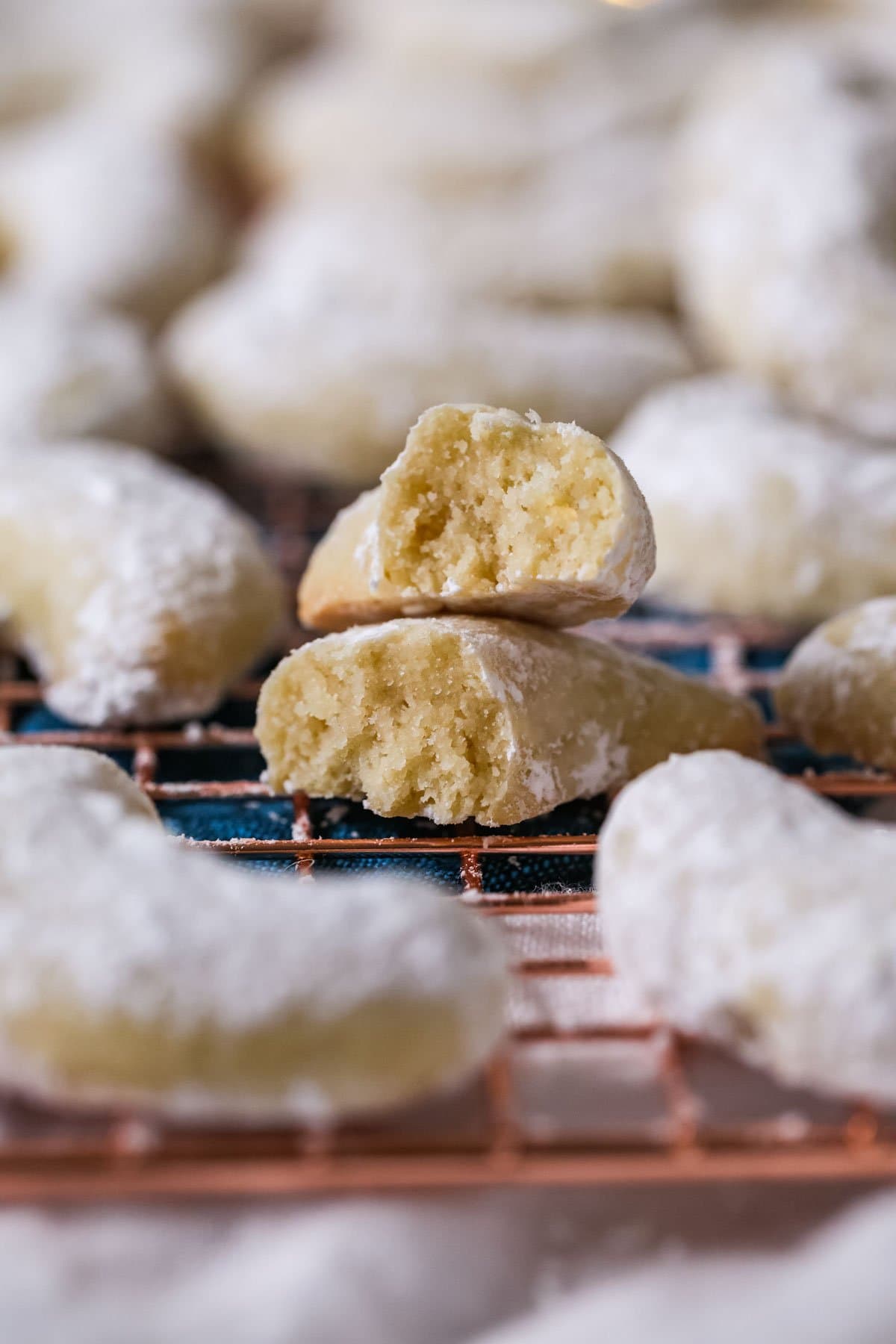Two halves of an almond flavored, powdered sugar dusted cookie stacked on top of each other.