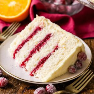 Slice of cranberry orange cake made with a cranberry sauce filling and orange cream cheese frosting on a plate.