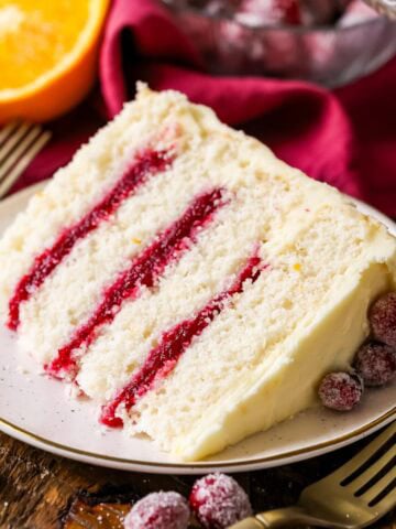 Slice of cranberry orange cake made with a cranberry sauce filling and orange cream cheese frosting on a plate.