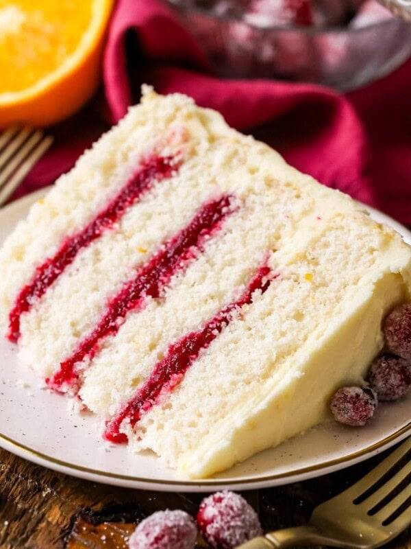 Slice of cranberry orange cake made with a cranberry sauce filling and orange cream cheese frosting on a plate.