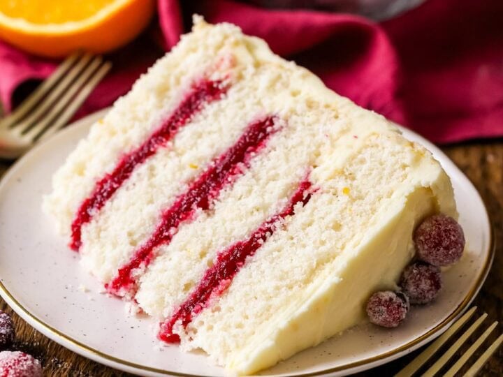 Slice of cranberry orange cake made with a cranberry sauce filling and orange cream cheese frosting on a plate.