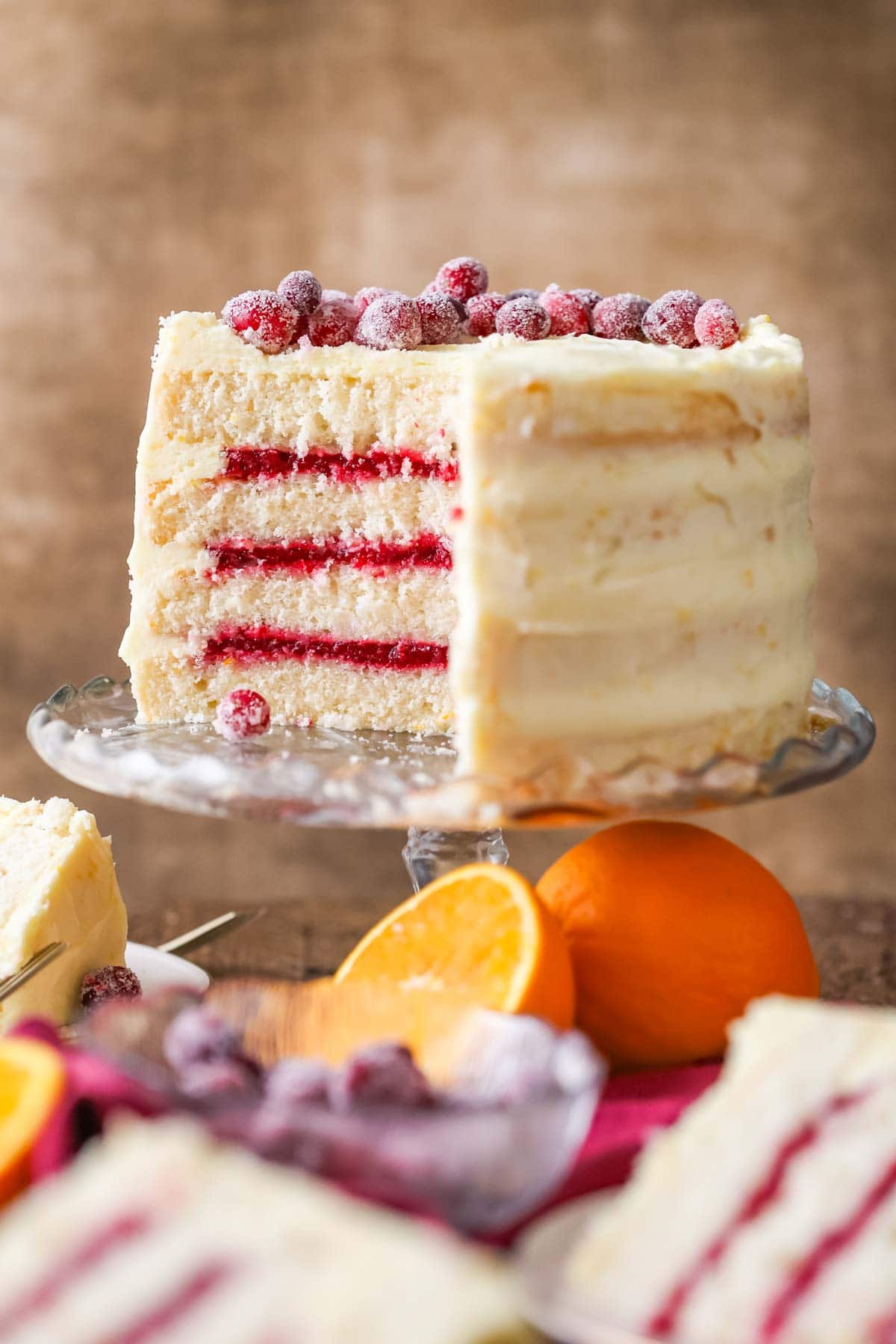 Cross section of a cranberry orange cake made with a cranberry sauce filling and orange cream cheese frosting on a cake pedestal.